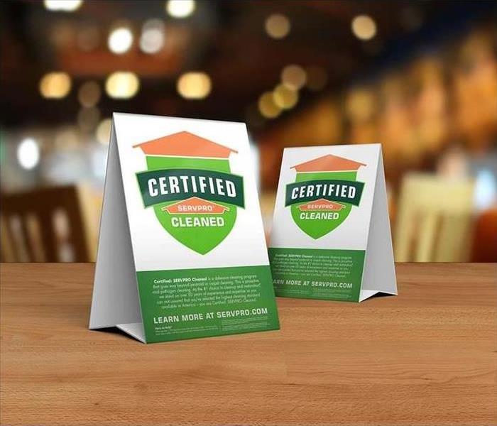 Table tent signs describing the Certified: SERVPRO Cleaned program on top of a wooden table.